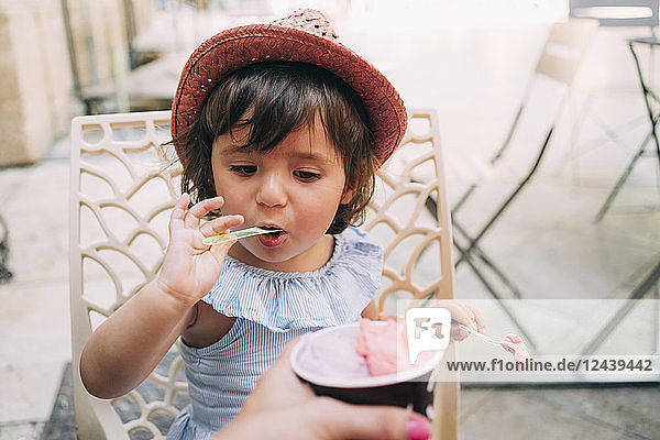 Cute toddler girl eating an ice cream held by her mother