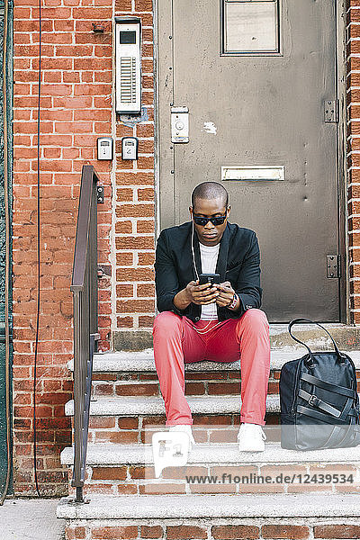 USA  NYC  Brooklyn  Man waiting on stairs  using smartphone