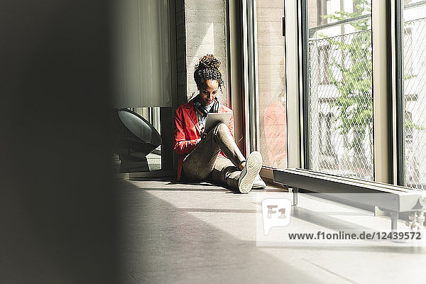 Young woman with headphones sitting on floor  using digital tablet