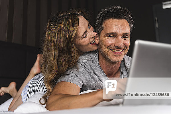 Happy couple lying on bed at home with laptop