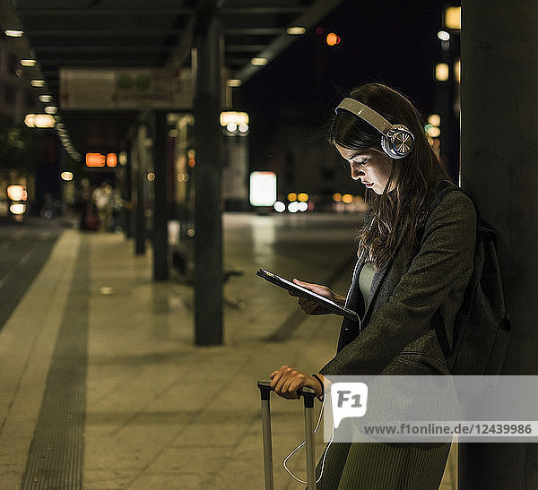 Young woman with headphones and tablet waiting at the station by night