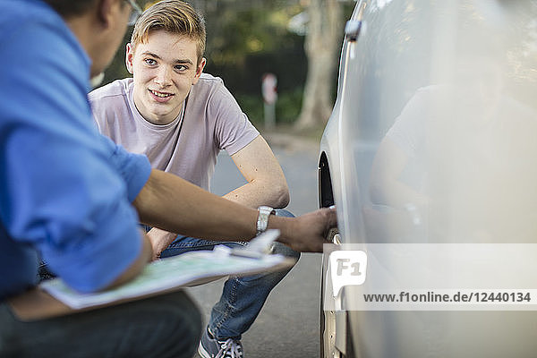 Learner driver with instructor checking tyre of a car