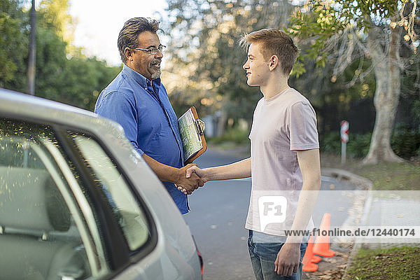 Learner driver and instructor shaking hands at car