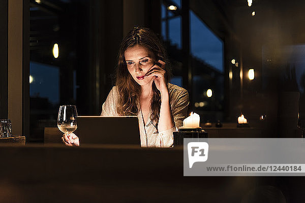 Woman having glass of white wine looking at laptop