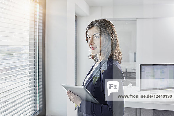 Smiling young businesswoman with tablet looking out of window in office