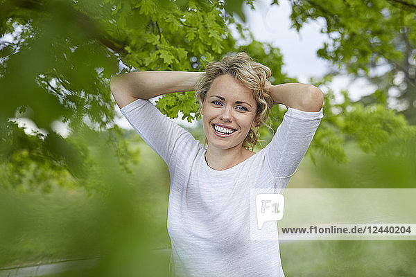 Portrait of relaxed blond woman with hands behind her head in nature