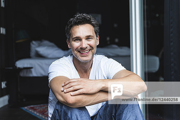 Portrait of smiling man in pyjama at home sitting at French window