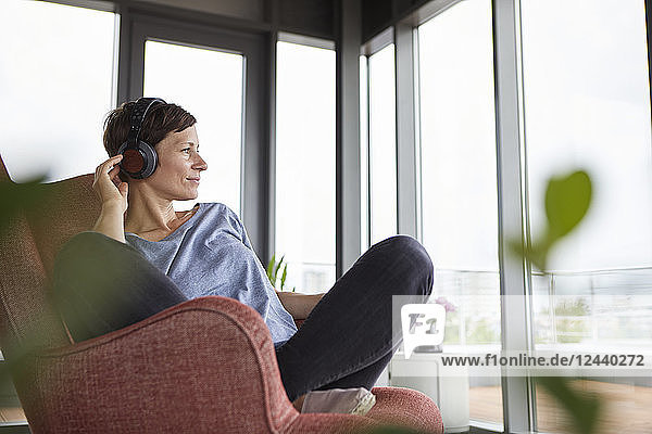 Woman sitting in armchair at home listening to music with headphones