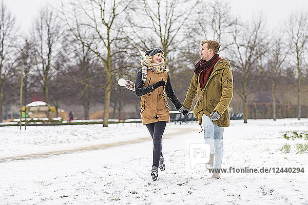 Happy young couple in love walking hand in hand in a park on snowy day