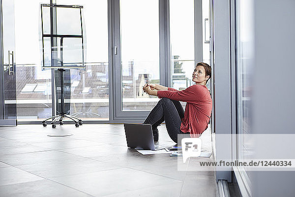 Businesswoman sitting on the floor in office with laptop and documents