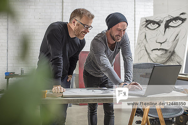 Smiling artist using laptop with man in studio