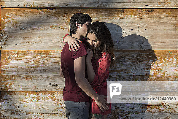 Affectionate young couple hugging and kissing at wooden wall