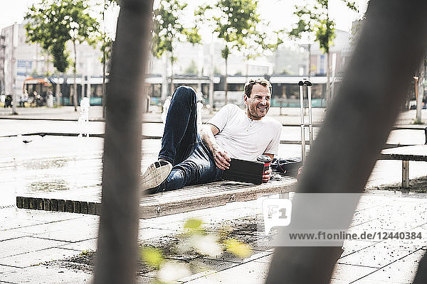 Smiling man lying on bench with tablet
