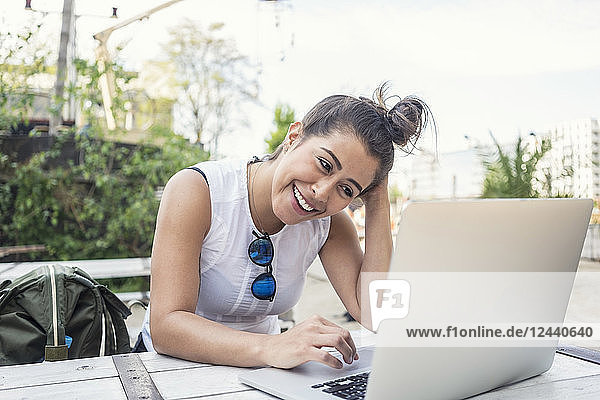 Portrait of laughing young woman using laptop outdoors