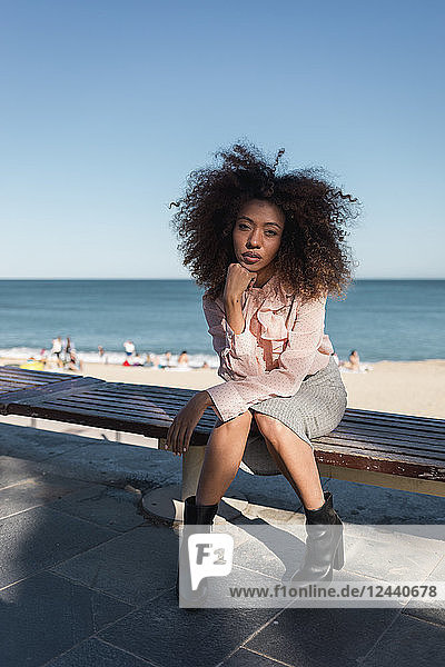 Portrait of beautiful young woman with afro hairdo sitting on a bench at the beach
