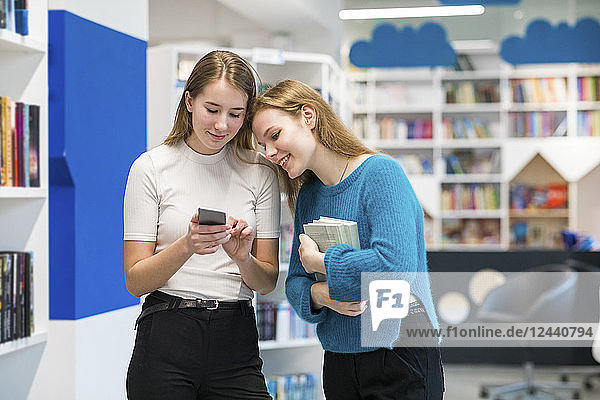 Two teenage girls in a public library looking at cell phone