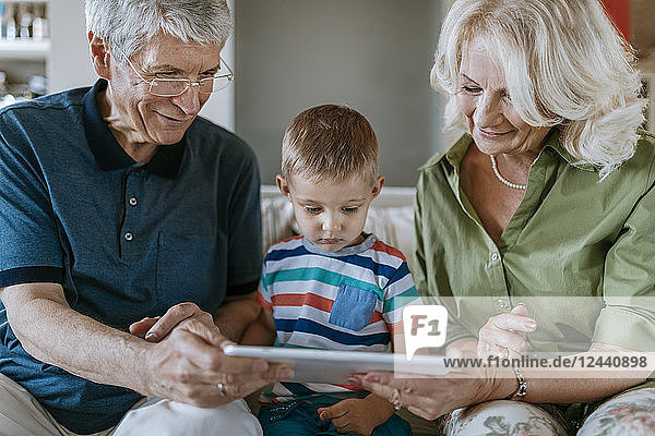 Grandparents and grandson at home sitting on couch sharing tablet