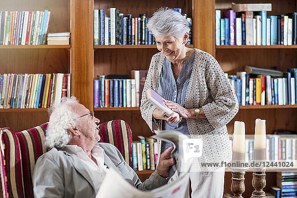 Senior man and woman sitting in library  reading book and newspaper