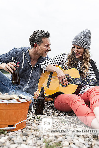 Happy couple with beer bottles  guitar and grill relaxing on pebble beach