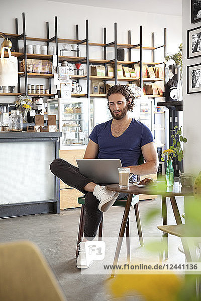 Portrait of young man sitting in a coffee shop using laptop