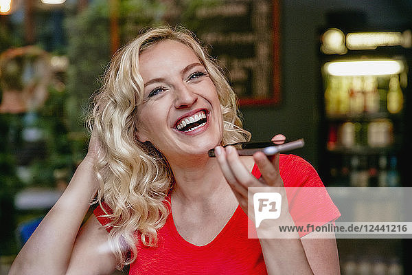 Portrait of laughing blond woman using smartphone in a cafe