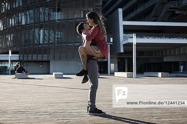 Young man lifting up happy girlfriend on city square