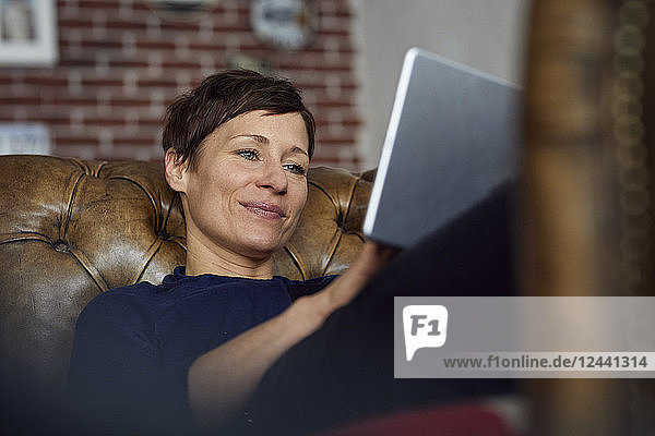 Woamn sitting on sofa at home  using digital tablet