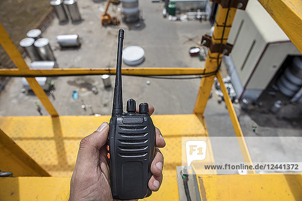 Hand holding walkie talkie on top of a crane on construction site