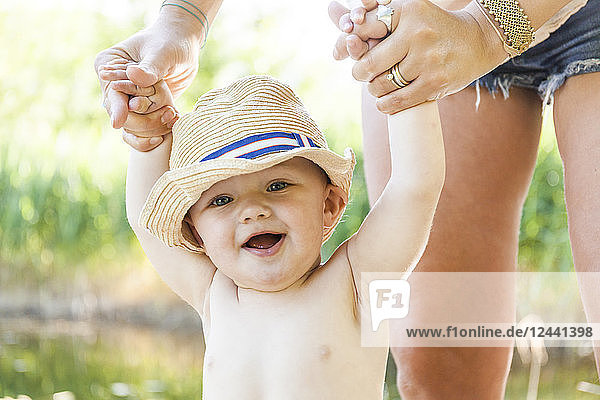Portrait of laughing baby boy holding his mother's hands