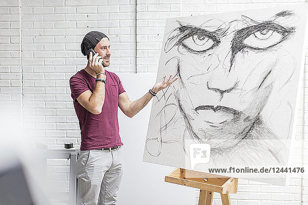 Artist on the phone in studio next to drawing