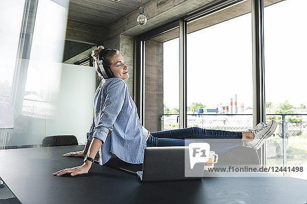 Young businesswoman sitting on desk  listening music