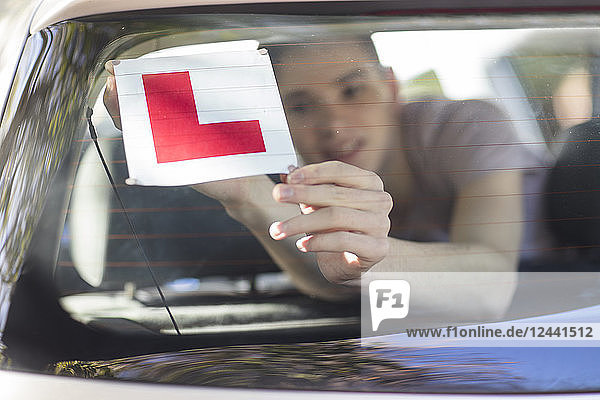 Learner driver placing letter L on rear window of car