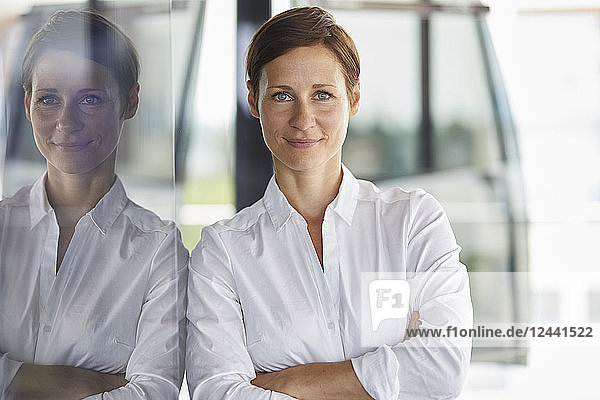 Portrait of smiling businesswoman leaning at glass pane in office