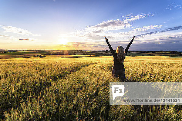 Back view of woman standing in grain field at sunset