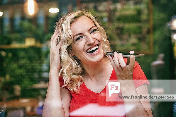 Portrait of laughing blond woman using smartphone in a cafe