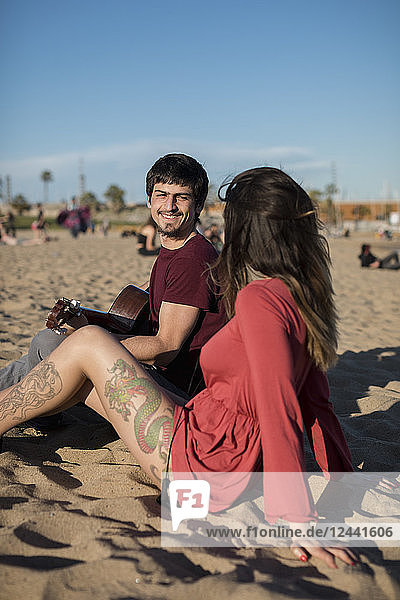 Spain  Barcelona  smiling couple with a guitar sitting on the beach