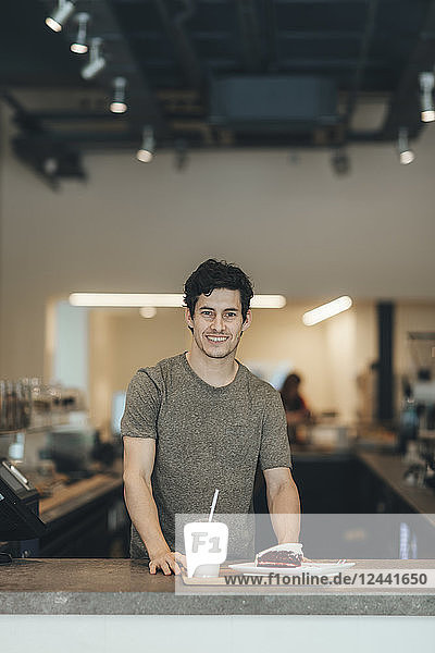 Portrait of smiling man serving drink and cake in a coffee bar