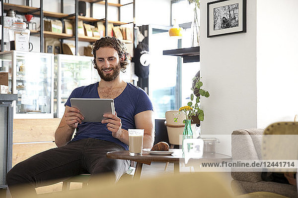 Portrait of young man sitting in a coffee shop using tablet