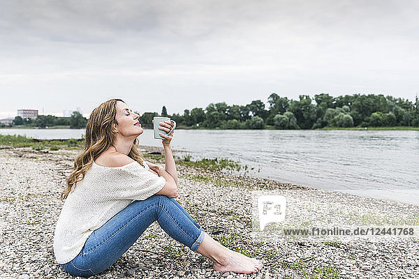 Woman sitting at the riverside enjoying cup of coffee