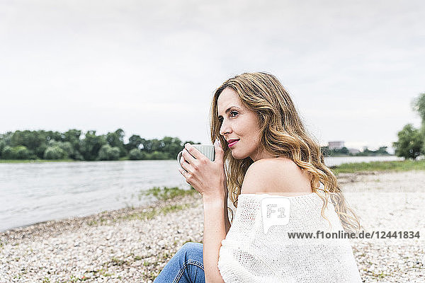 Woman sitting at the riverside drinking cup of coffee