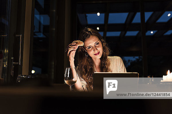 Smiling woman having dinner looking at laptop
