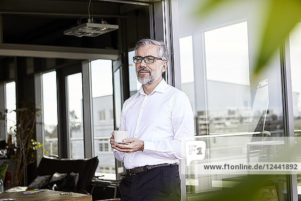 Businessman standing at French door with cup of coffee