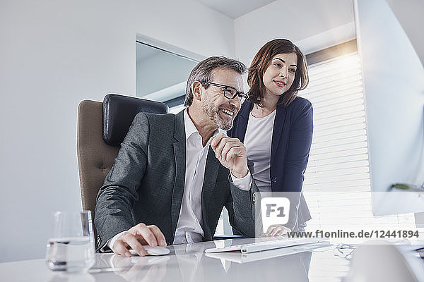 Smiling businessman and businesswoman looking at computer at desk in office