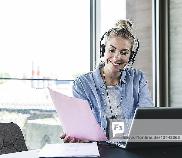Young businesswoman sitting at desk  making a call  using headset and laptop