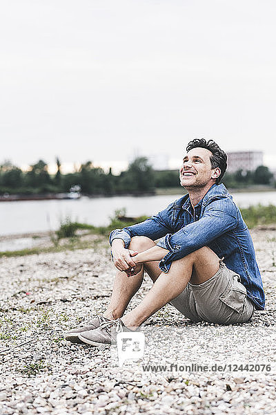 Smiling man sitting at the riverside looking up
