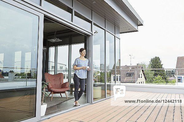 Woman at home with cup of coffee looking on roof terrace