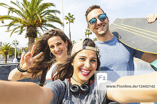 Selfie of three happy friends with skateboard