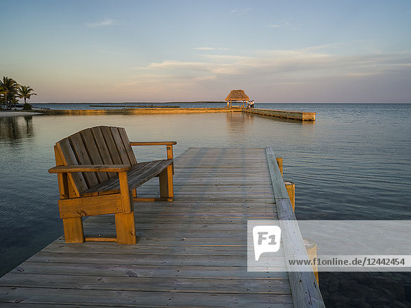A wooden bench on a dock and open ocean at sunset; Belize