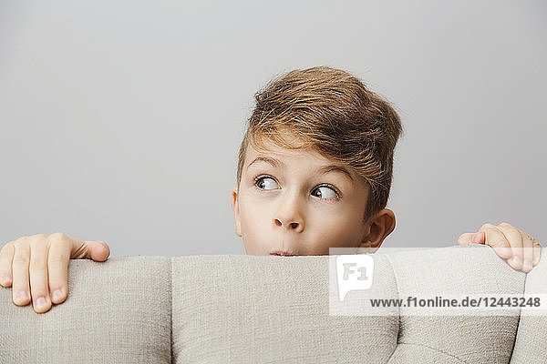 Porträt eines kleinen Jungen  der mit einem dummen Gesichtsausdruck hinter einer Couch hervorschaut; Langley  British Columbia  Kanada