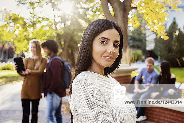 A young female university student of Lebanese ethnicity poses while her friends talking are together in the background on the university campus  Edmonton  Alberta  Canada